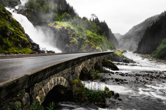 Water of a waterfall is flowing from a mountain under a long bridge into a wild mountain river in Norway at the famous Latefossen