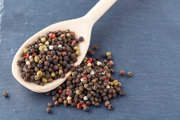 Top view on composition of peppercorns in wooden spoon on dark background, close-up.