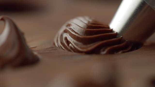 closeup of pastry bag filling candy mold form with chocolate cream. Side view macro