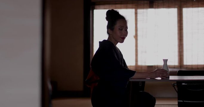 Japanese woman wearing Kimono by traditional window drinking Saki, Kyoto Japan