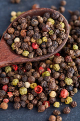 Top view on composition of peppercorns in wooden spoon on dark background, close-up.