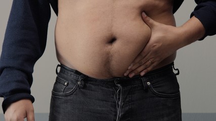 Naklejka premium overweight man closeup of belly front view. put up shirt and pinch and clap a belly