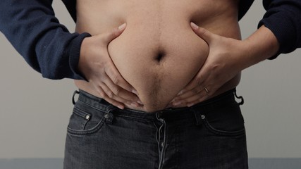 Naklejka premium overweight man closeup of belly front view. put up shirt and pinch and clap a belly