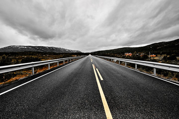Fototapeta premium Remote road leading through the wilderness of Norway with asphalt , forest and mountains on a dark cloudy sky