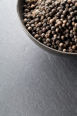 Raw, natural, unprocessed black pepper peppercorns in black bowl