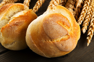 Bunch of whole, fresh baked wheat buns with wheat ears on dark wooden table