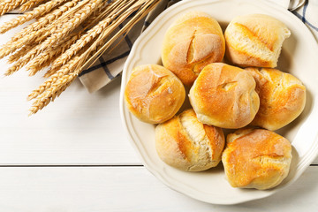 Bunch of whole, fresh baked wheat buns with wheat ears on white wooden table