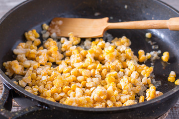 Frozen sweet corn in a frying pan on a wooden table