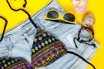 Summer vacation concept, flatlay jeans shorts, bikini, leather bracelet, yellow sunglasses and sea...