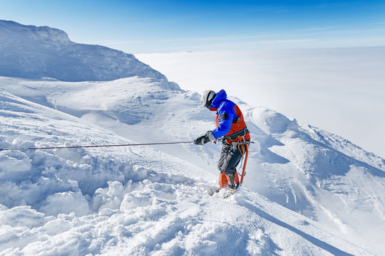 Equipped climber ascent by snowy slope with climbing rope on the top of peak in snowy alpine mountains. Life guard professional man on the work in high mountains. Action in hard conditions scene.