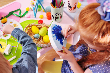 children in kindergarten paint eggs for the Easter basket at the table.