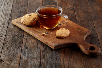 Cup of tea with cookies on a cutting board on a wooden background, top view