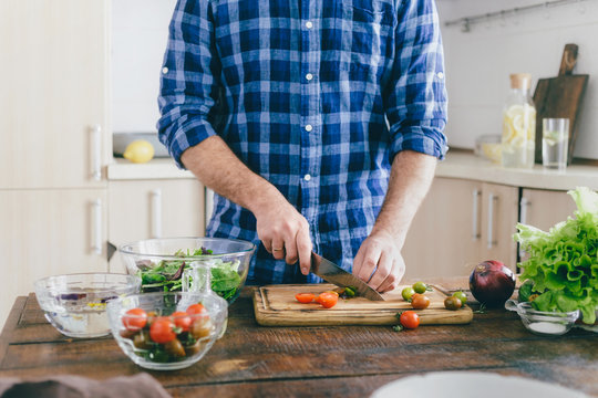 Man cooking summer salad of vegetables on wooden table in home kitchen
