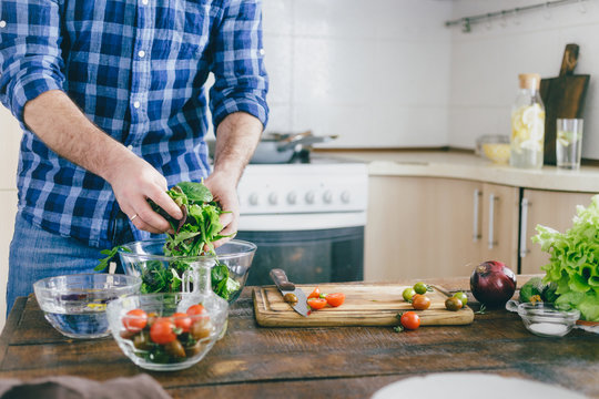 Man cooking summer salad of vegetables on wooden table in home kitchen. Copy space