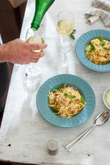 Plate homemade spaghetti carbonara with glass of white wine on white wooden table, top view