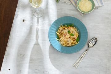 Plate of pasta carbonara with glass of white wine on white wooden table, top view. Dinner table concept