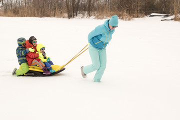 A happy mother with kids in sunglasses and a bright blue ski suit. Mother and children are happy together. A sports family on a snow-covered river with snow. Boys are very happy to play outdoors