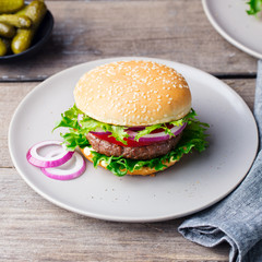 Burger on a plate with pickles. Wooden background.