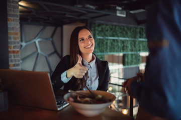 Woman is sitting in the restaurant and shows thumb up to waiter.