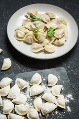 Traditional russian pelmeni, ravioli, dumplings with meat on black concrete background