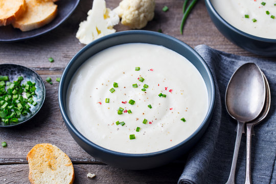Cauliflower and potato cream soup with green onion in a bowl on grey wooden background.