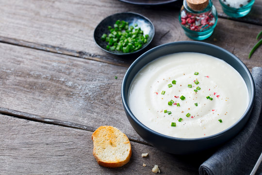 Cauliflower and potato cream soup with green onion in a bowl on grey wooden background. Copy space.