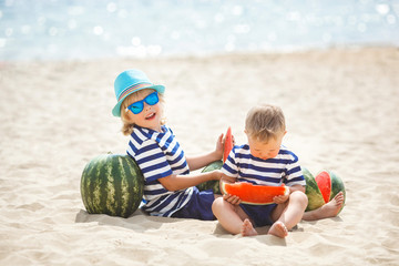 Two adorable children sitting at the sea shore and eating watermelon. Two brothers having fun on...