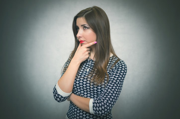 Pensive wistful woman is wondering and thinking isolated on gray background. Disappointed girl.