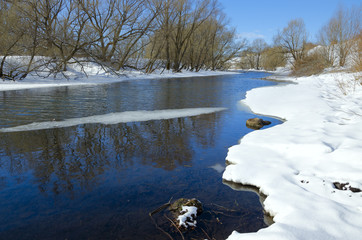 Springtime.Sunny landscape with  trees growing on the bank of river.Melting snow and ice.White...