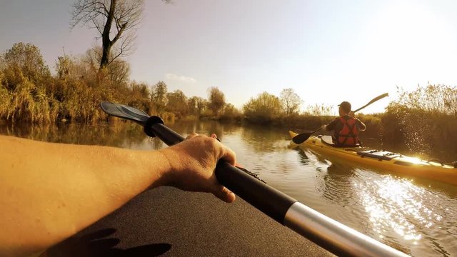 POV shot of kayakers paddling down the river in yellow and red kayak in amazing landscape on a beautiful sunny day.
