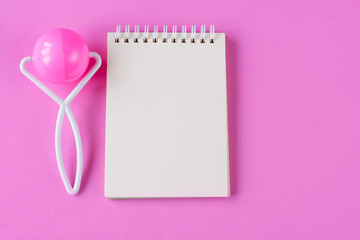 Notepad and baby rattle on pink background. Space for text