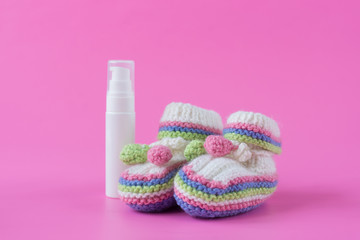 Baby's bootees and .bottle of cream on pink background. Space for text