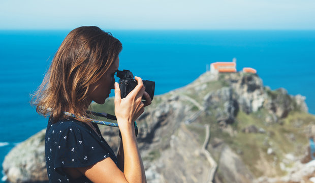 Tourist traveler photographer making pictures sea scape on photo camera on background ocean gaztelugatxe steps on Spain, hipster girl looking on nature horizon, relax holiday