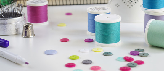 Spools of thread and basic sewing tools including pins, needle, a thimble and buttons. Copy space. Long banner format