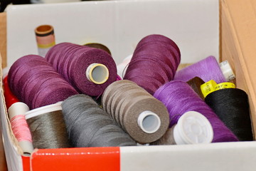 Purple, brown and black threads in a roll and coils lie in a box, close-up.