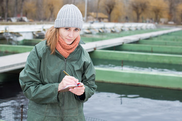 Female worker of fish farm writing something in notebook