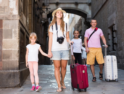traveling family of four strolling with luggage along European city street