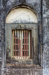 Fototapeta na wymiar Madikeri, India - October 31, 2013: Closeup of window and rusty decorated metal frame of Royal mausoleum, set in white wall devastated by black mold. Hindu figurines.