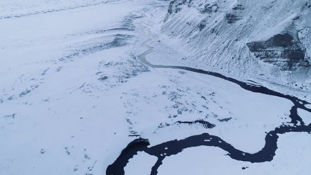 Pristine aerial shot flying over winter landscape: a creek winding along side of a mountain. Snow covered land at dawn.