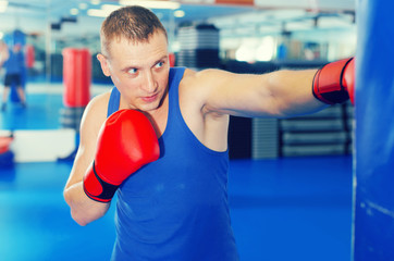 Active male is training with punching bag in box gym