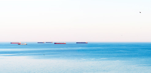 Fototapeta na wymiar Sea summer panorama. Early morning, Cargo ships in the roadstead. Sunrise, wind on the water. Horizontal panoramic view