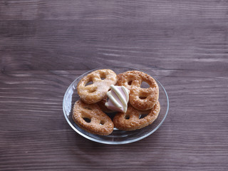 Homemade cookies and marshmallows on a transparent glass plate on a wooden table