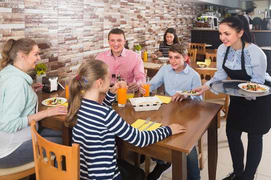 Young brunette waitress serving family in family cafe