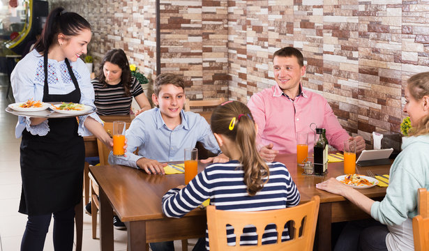 Polite pretty waitress bringing ordered dishes to family