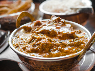 Indian Food or Indian Curry in a copper brass serving oriental bowl, pieces of chicken fillet in curry sauce ingredients in a pan with the old table side view close-up, Set of Indian food.