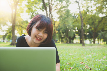 Young asian woman's legs on the green grass with open laptop. Girl's hands on keyboard. Distance learning concept. Happy hipster young asian woman working on laptop in park. Student studying outdoors.