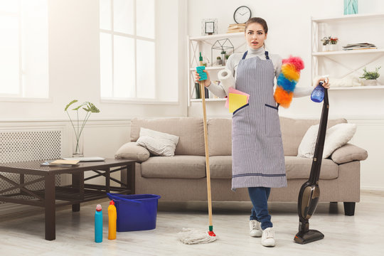 Shocked woman cleaning house with lots of tools