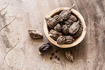 Black cardamom in a bowl on wooden background top view
