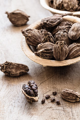 Black cardamom in a bowl on wooden background