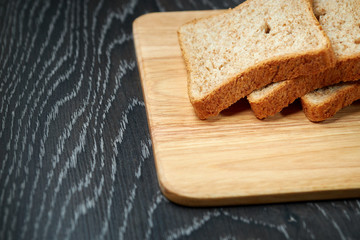 Sliced bread on wooden cutting Board, on dark wooden background, bran